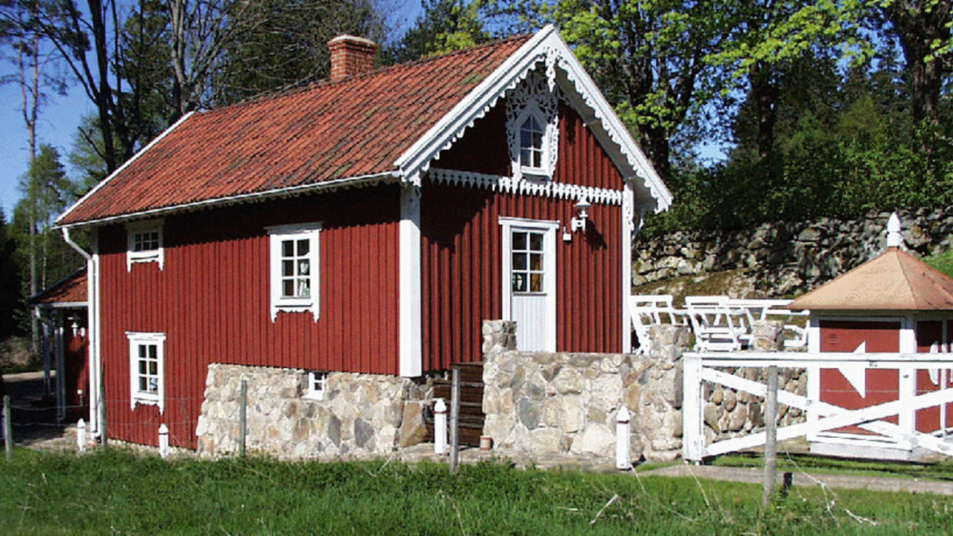 Röd stuga med vita knutar och snickarglädje.