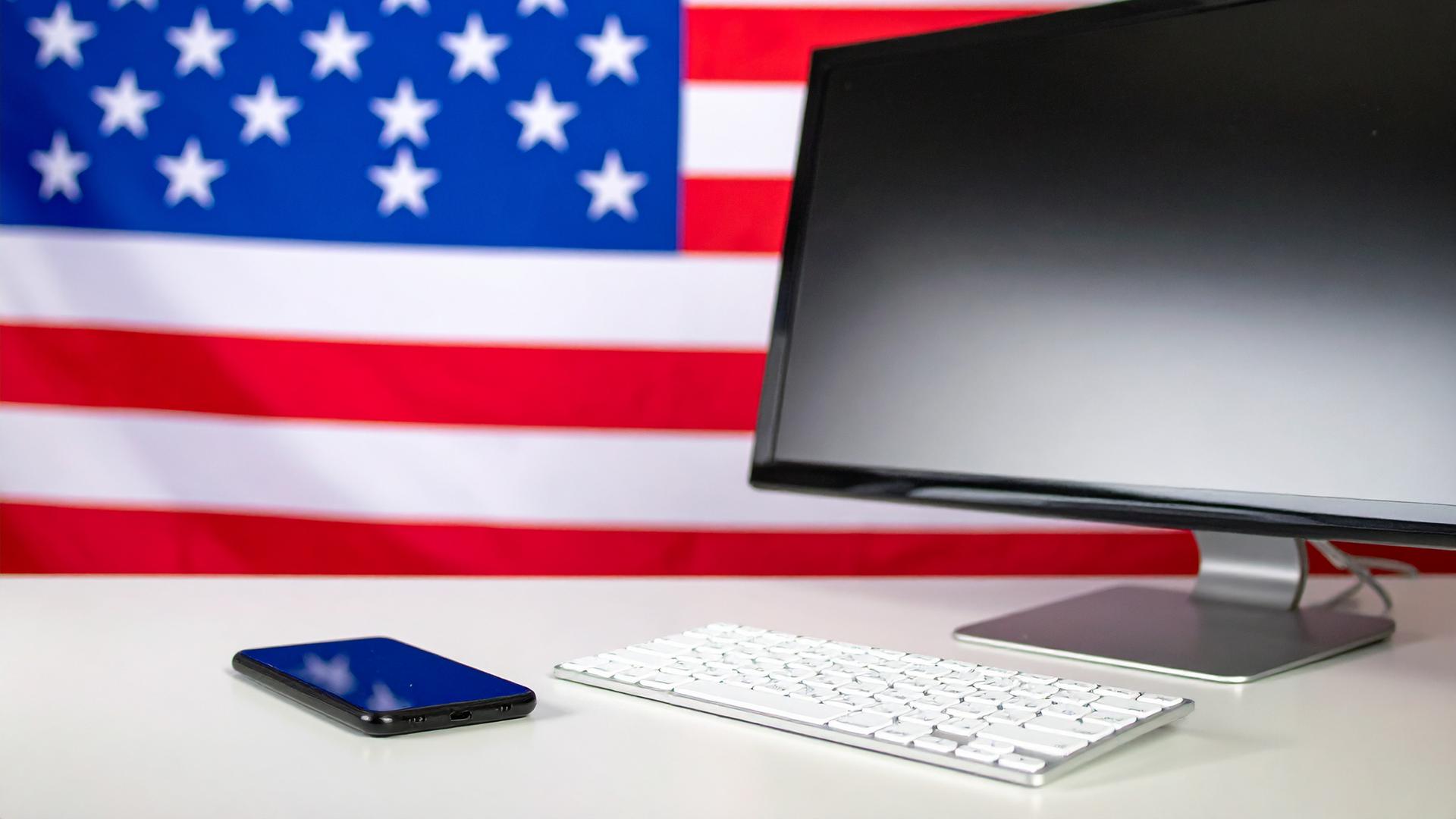 mobiltelefon och dator på ett bord. bakom syns usas flagga