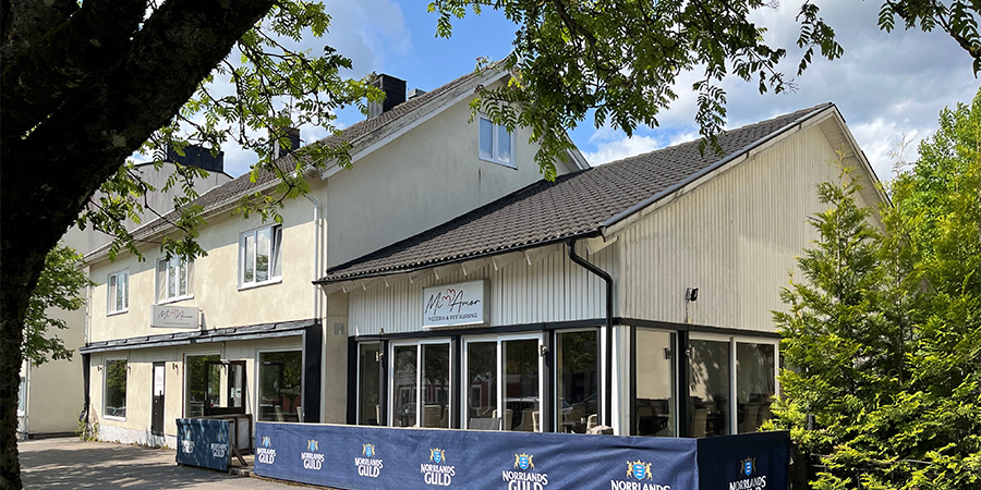 Ljus putsbyggnad med glaspartier och uteservering.