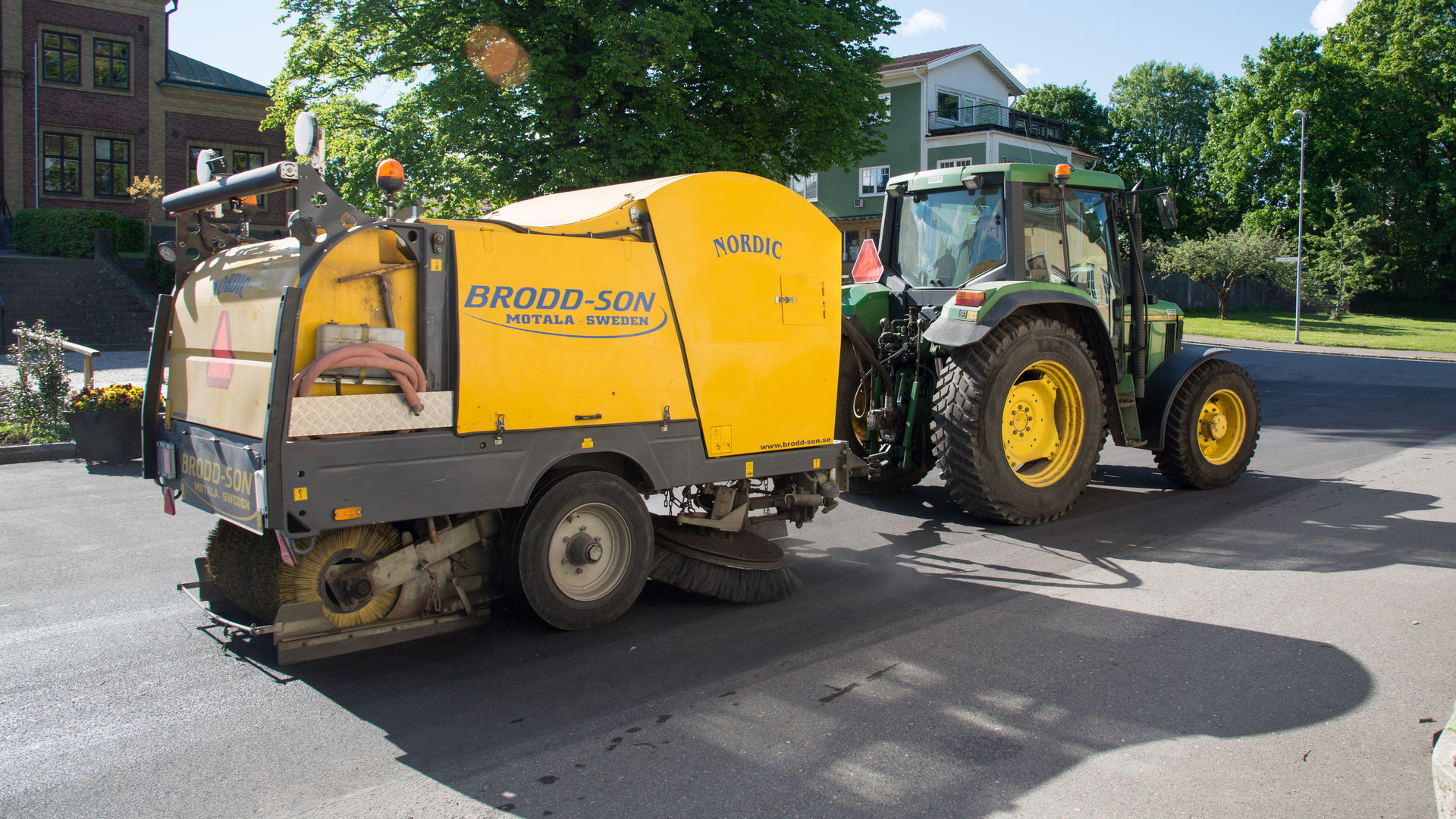 traktor med en sopningsmaskin bakom, sopar en gata