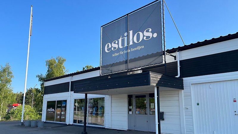 Vit butiksbyggnad med stor skylt "Estilos"