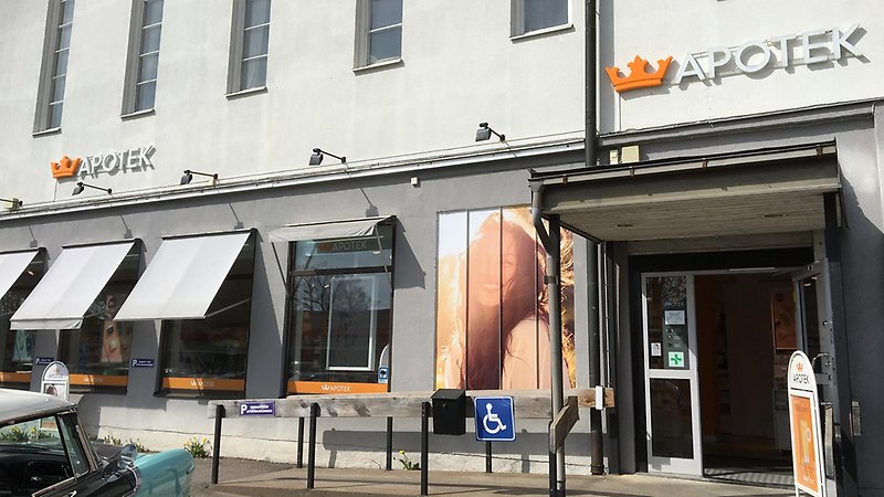 Vit byggnad med skyltfönster och dörr, skylt Apotek