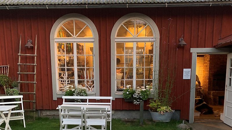 Röd stuga med stora välvda fönster, trädgårdsmöbler utanför