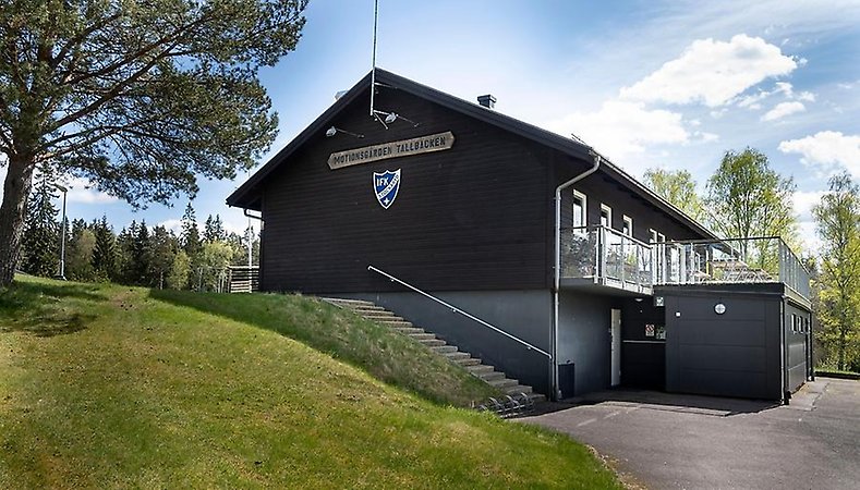 Mörkbrun träbyggnad på grässlänt. Klubbhuset på Tallbacken.