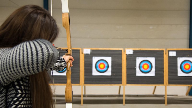 Kvinna skjuter pilbåge mot tavla.