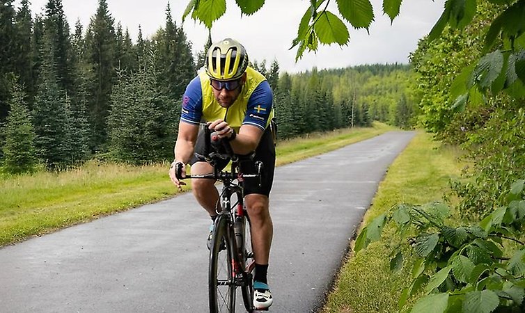 En man cyklar på asfalt i skogslandskap.