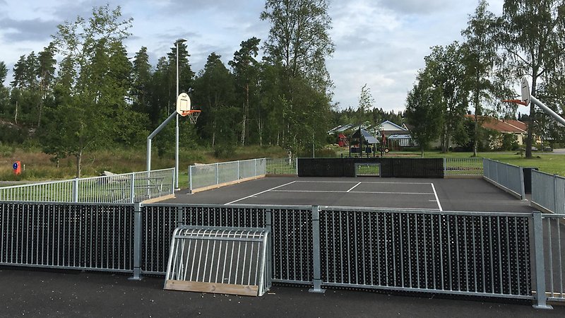 Asfalterad bollplan med staket runt. Basketkorg, bandymål.
